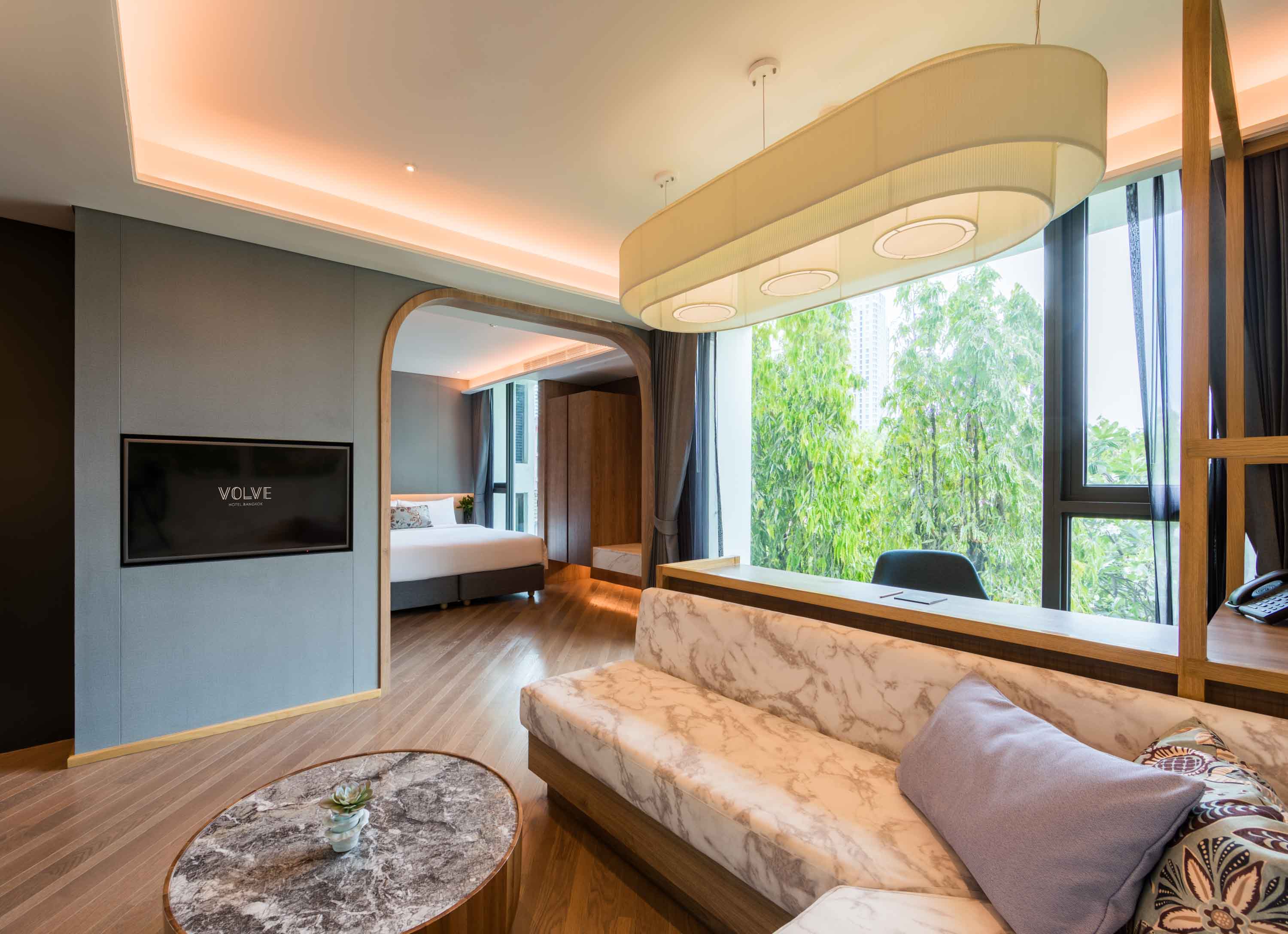 Marble print sofa, large work table and lush garden view in the Studio Suite at Volve Hotel Bangkok